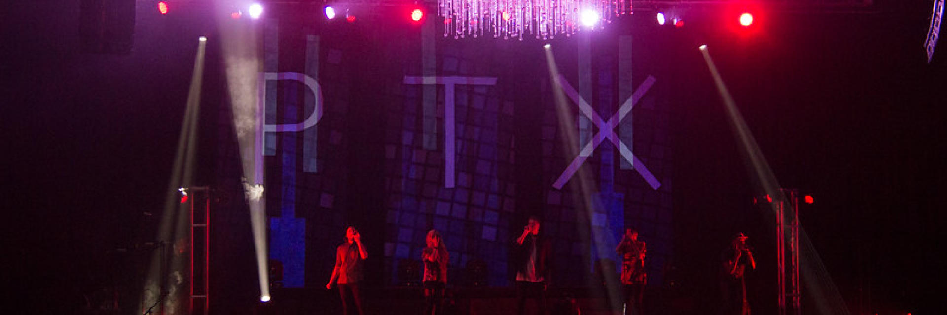 Pentatonix, a five member acapella group, in a dark room being illuminated with red and purple lights.